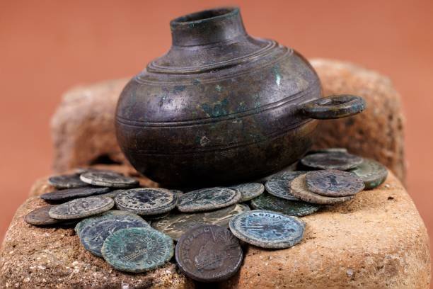 Ancient coins and a bronze pot displayed on stone, showcasing historical artifacts.